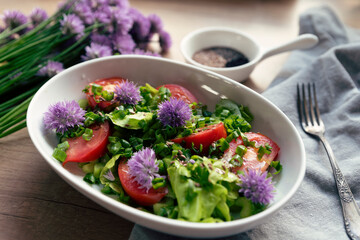 Salad for breakfast. Vegetarian meal with vegetables, lettuce, tomatoes and flowers of chives, Sping in a kitchen, on a table and bowl. Close up.