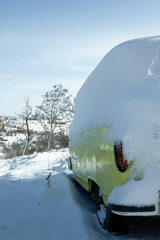 A yellow-white minibus covered with a snowdrift. Among the snowdrifts around
