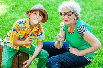 Happy grandmother and grandchild hold dandelions pretending to be singing into a microphone. Older...