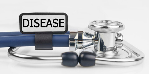 On the white surface lies a stethoscope with a plate with the inscription - DISEASE