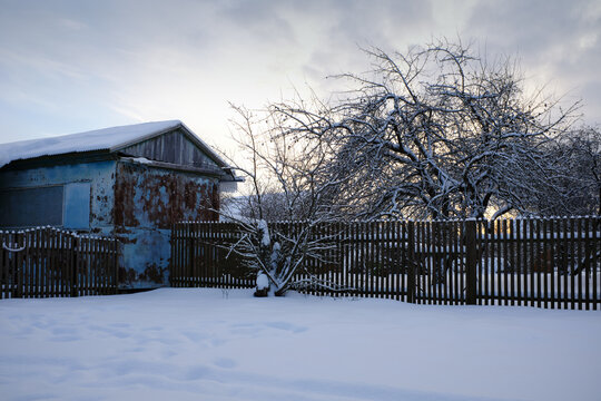 Winter photography. A blue, iron shed surrounded by a fence.