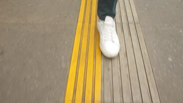 Legs in white sneakers take steps along the yellow line. Security border at the train station. The passenger moves along the line.