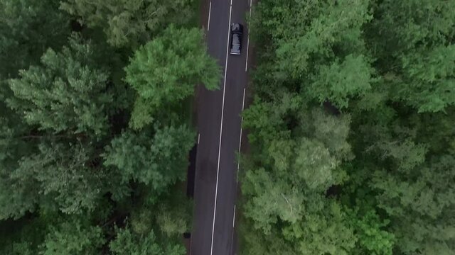 Drone top view camera tracking black car driving very fast on empty highway along cloudy autumn forest on atmospheric road trip. Aerial view. 4K Footage