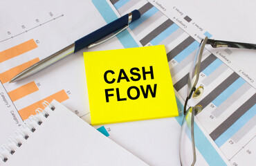 Yellow sticker with text Cash Flow lies on financial charts with pen and eyeglass