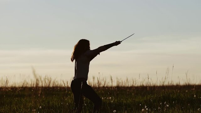 A man with long hair armed with a knife trains and practices blows in nature at sunset. Cool shots