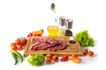 Raw veal steak on a wooden cutting board. Olive oil, juicy fresh vegetables and herbs.