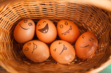 Stack of eggs with hand drawn faces on straw basket, easter preparation, holiday mood concepts