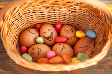 Stack of eggs with hand drawn faces on straw basket with colorful candy, easter preparation, holiday mood concepts