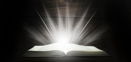 Open Bible. Rays of light come down from the book. The Holy Book. On a wooden table
