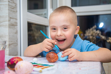 A boy with Down syndrome draws, a genetically ill child paints Easter eggs, preparation for Easter,...
