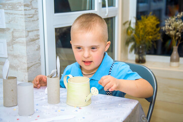 A boy with Down syndrome watering a plant from a watering can, a disabled child.

