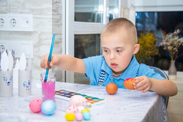A boy with Down syndrome draws, a genetically ill child paints Easter eggs, preparation for Easter,...