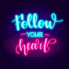 Follow your heart. Glowing pink neon incription on dark brick wall background.