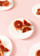 Pieces of red oranges fruit on a white plate on a pink background