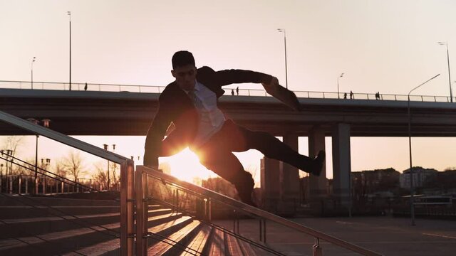 Businessman in jacket and tie with a suitcase in his hands jumps over an obstacle on background city in the sunset light. Office worker makes a trick through parapet. Concept overcoming difficulties.