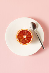 Obraz na płótnie Canvas Red orange fruit on a white plate on a pink background