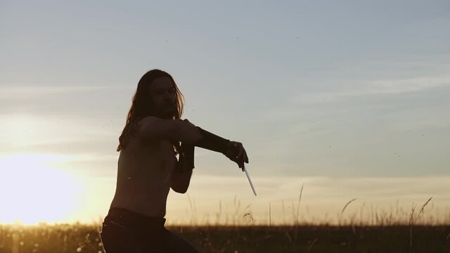 In the evening, at sunset, a warrior with a knife in his hands practices combat techniques. Very cool silhouette.
