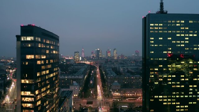 Cinematic drone shot of a night city with skyscrapers and roads with cars in winter in Warsaw. Poland. A drone flies between two skyscrapers at night overlooking a multi-lane road with traffic 