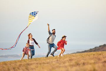 Happy family father,  mother and children launch  kite on nature at sunset