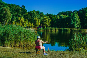 An elderly woman sunbathes in the sun near the lake.