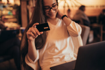 Young woman millennial sitting in a coffee shop and shopping online using her laptop and credit card.