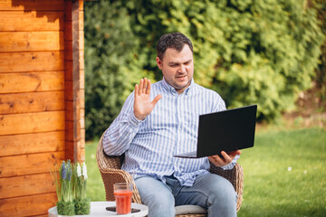 Fototapeta premium Businessman working on laptop in his own garden. Home office in spring and summer. Telecommunications during the pandemic. Stay at home, work on vacation 
