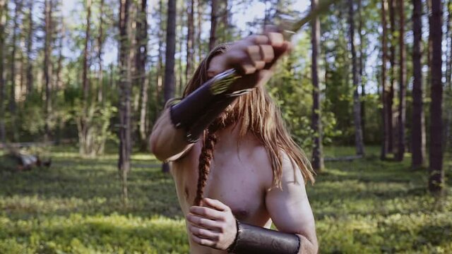 A warrior with a large knife in the forest strikes while looking at the camera. Aggressive guy