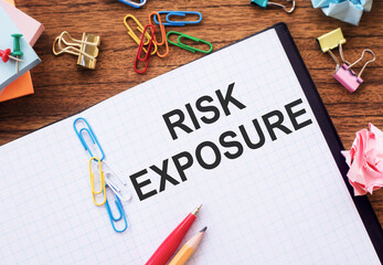 Notepad with the text RISK EXPOSURE on the table with colored paper clips and crumpled sheets.