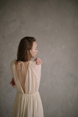 Fototapeta na wymiar Young beautiful woman wearinng white vintage dress posing near textured wall.