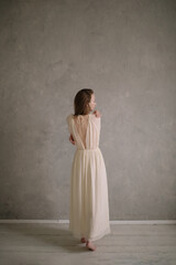 Young beautiful woman wearinng white vintage dress posing near textured wall.