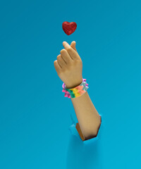 K pop concept. A girl hand with rainbow pyramid studded bracelet showing fingers heart gesture. Red glittery heart above. Optimistic blue in background.