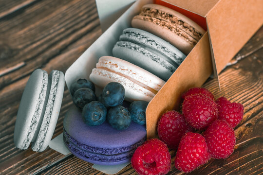 Close-up. Blueberries, raspberries and colored macaroon cookies in a cardboard box on a wooden background