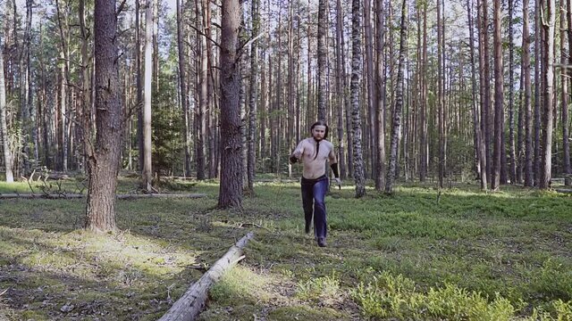 The knife-wielding hero runs bare-chested through the woods toward the camera. He's chasing someone.