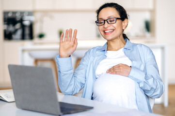 Online meeting concept. Successful pregnant mixed race woman, coworker, business lady uses laptop,...