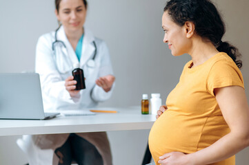 Doctor advises and prescribes medications for the pregnant woman. Mixed race, mature pregnant woman, sitting at the doctor's appointment, undergoing medical prevention and treatment.Healthcare concept