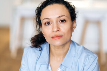 Close-up portrait of serious successful confident beautiful brunette mixed race business lady, in blue formal shirt, looking at camera