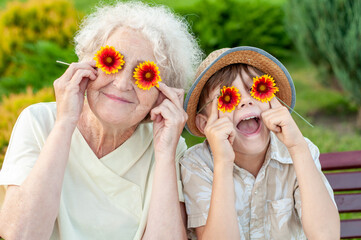 Boy and grandmother puts on the eyes of chamomile. Family holiday.Laughing grandson with his...