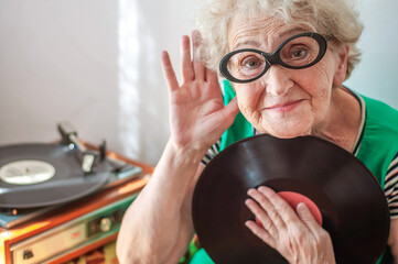 Elderly woman with glasses listens to vinyl records on a turntable. Retro music. Grandma is...