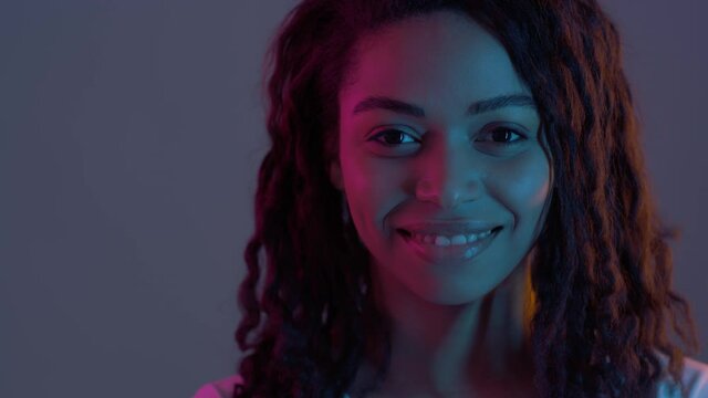 Playful african american lady turning face to camera and winking happily in neon light, slow motion