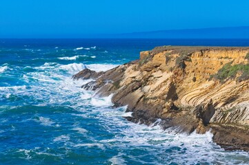Ocean waves crash into the California coast creating interesting textures in the rocks face.