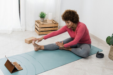 African senior woman exercising while doing online yoga class at home - Sport and healthy lifestyle concept - Focus on face