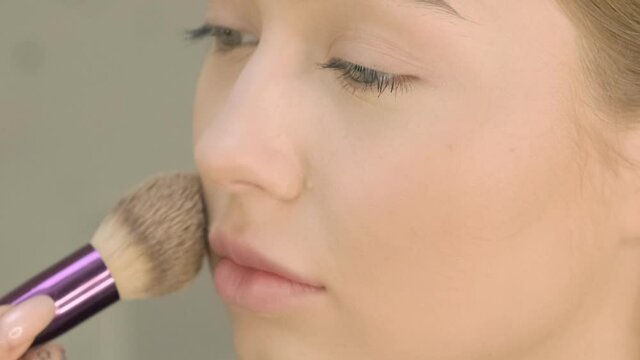 Preparing the model`s skin for applying makeup. Processing the face with a brush with a powder Foundation applied. Makeup artist is painting lips contour using pencil for woman, closeup view