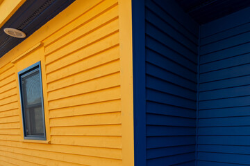 A closeup of the exterior corner a colourful yellow and blue wooden textured horizontal clapboard country style house. The clean lines in the building are made of wide textured pine boards. 