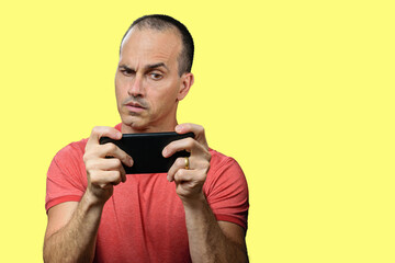 Mature man in casual clothes, suspicious and holding smartphone horizontally.