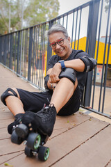 The happy latin old man with a roller skates sitting on the asphalt