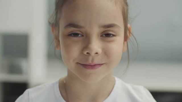 Large portrait of a small brown-eyed smiling girl in a white T-shirt