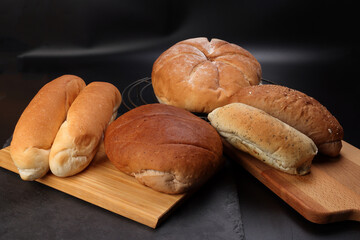 Freshly baked bread loaf bun roll round long mix verity on wooden board metal grill over black background
