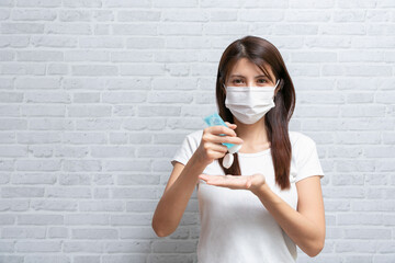 Asian woman in medical protective mask applying an antibacterial antiseptic hand gel for hands.