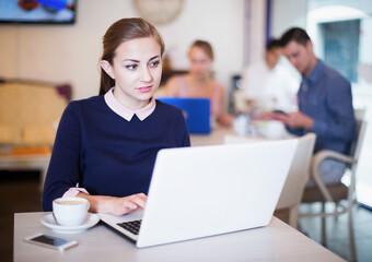 Young female spending time in cozy confectionery with laptop and coffee
