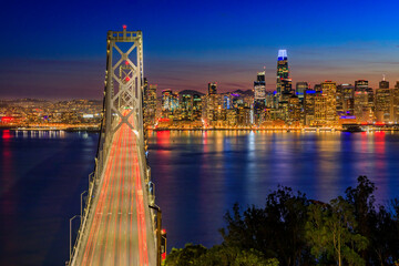 Bay Bridge with light trails and downtown San Francisco viewed from Treasure Island at sunset and reflections on the water in the Bay, long exposure